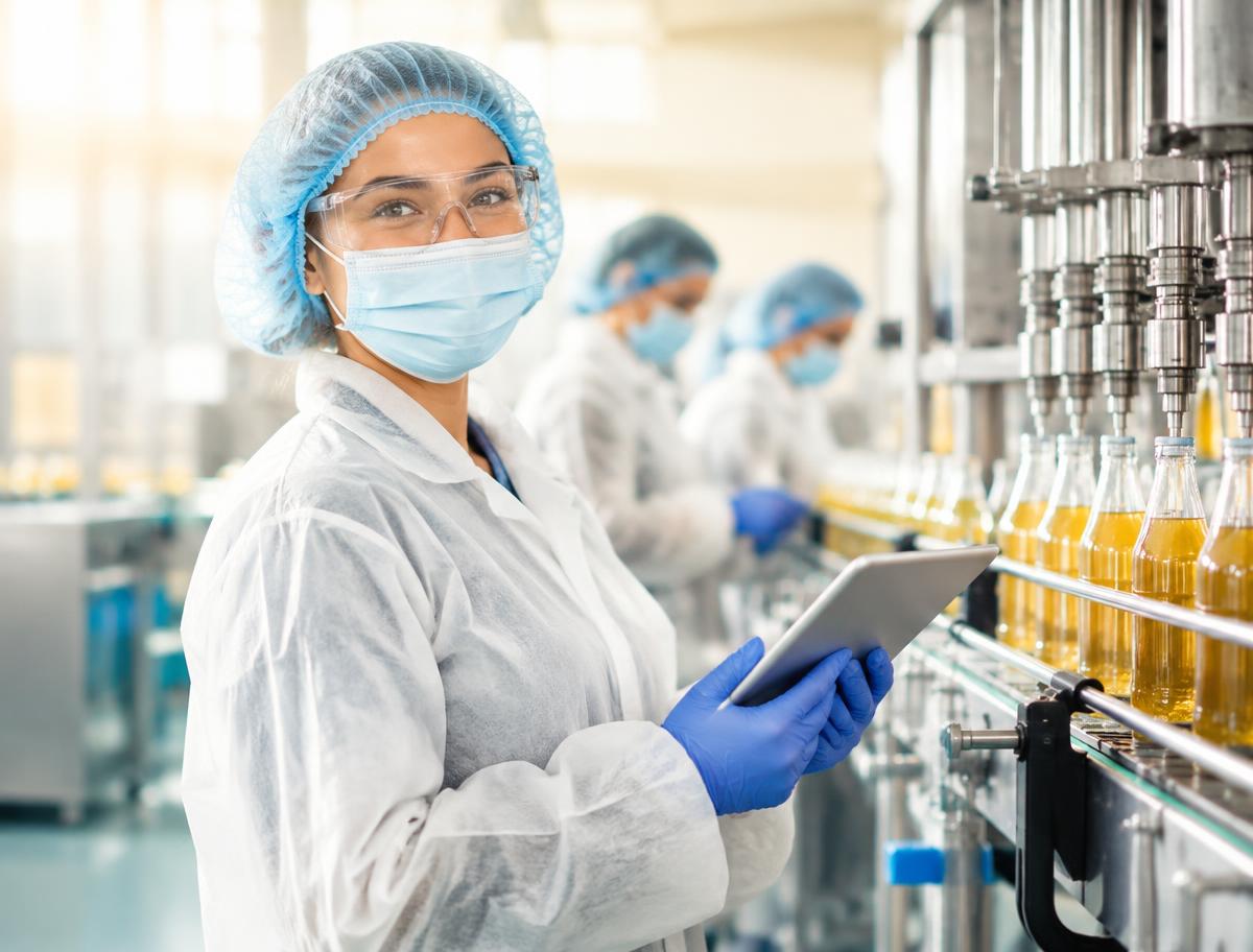Smiling beverages & liquid manufacturing team member in full protective clothing using a tablet on the production floor