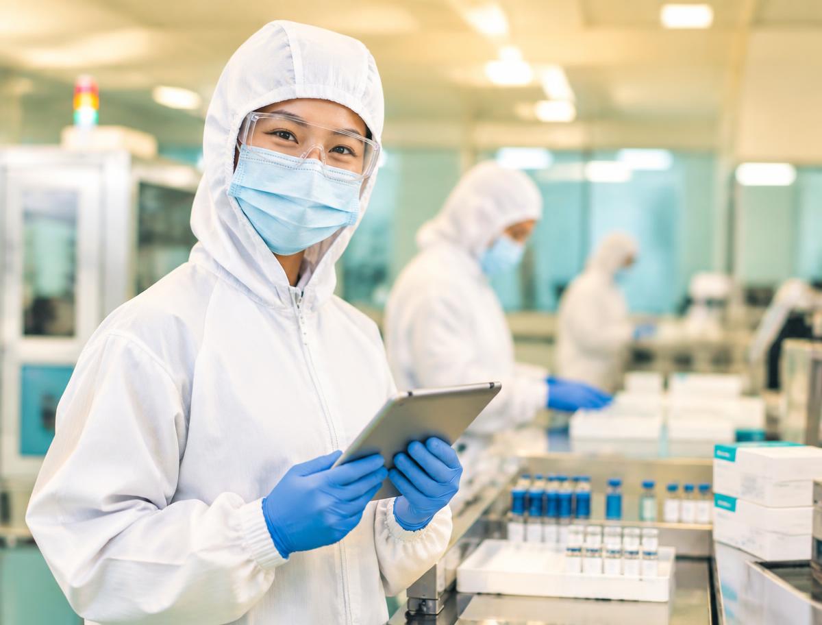 Smiling diagnostics & ivd kits team member in full protective clothing using a tablet on the production floor