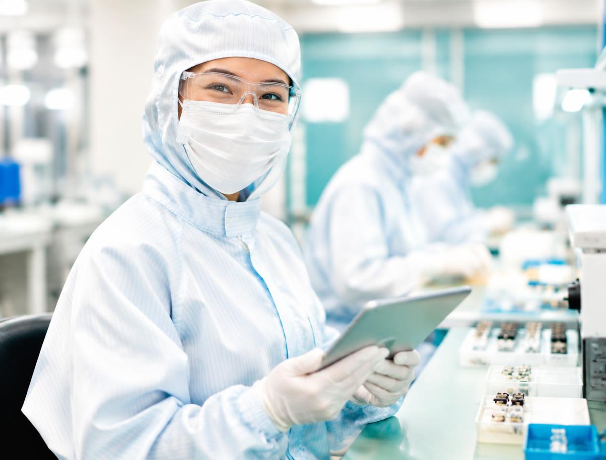 Smiling medical devices team member in full protective clothing using a tablet on the production floor