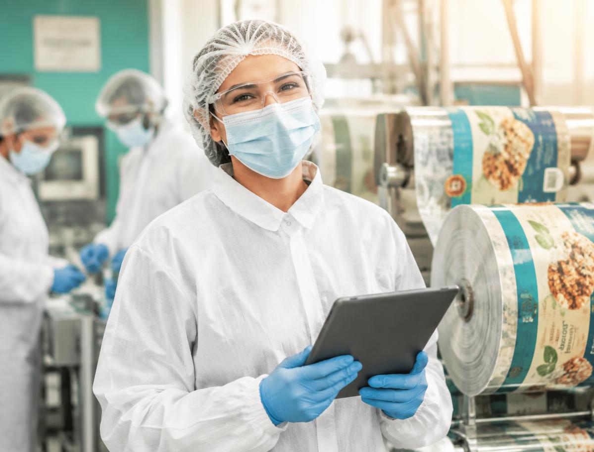 Smiling packaging & food-contact materials team member in full protective clothing using a tablet on the production floor