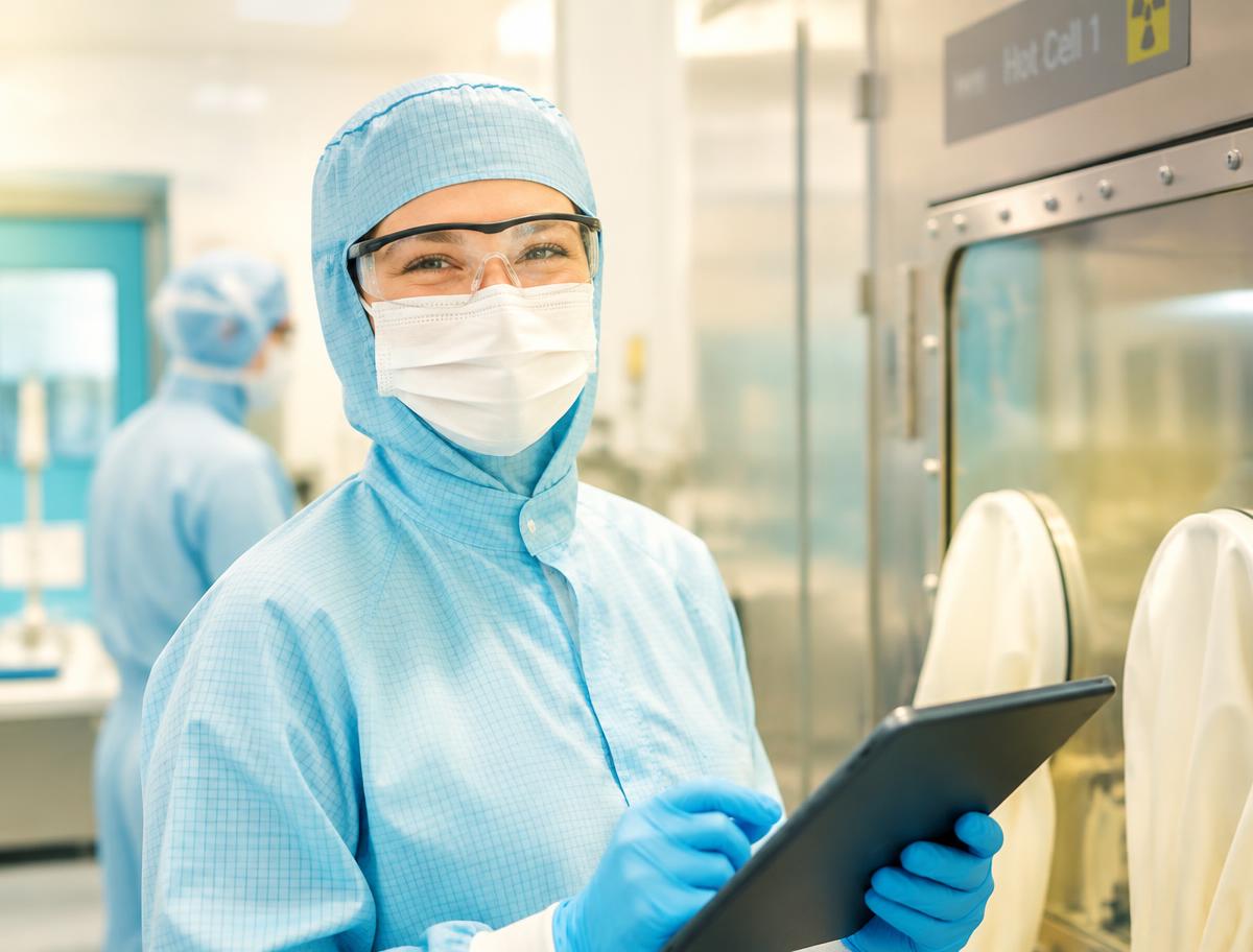 Smiling radiopharmaceuticals team member in full protective clothing using a tablet on the production floor
