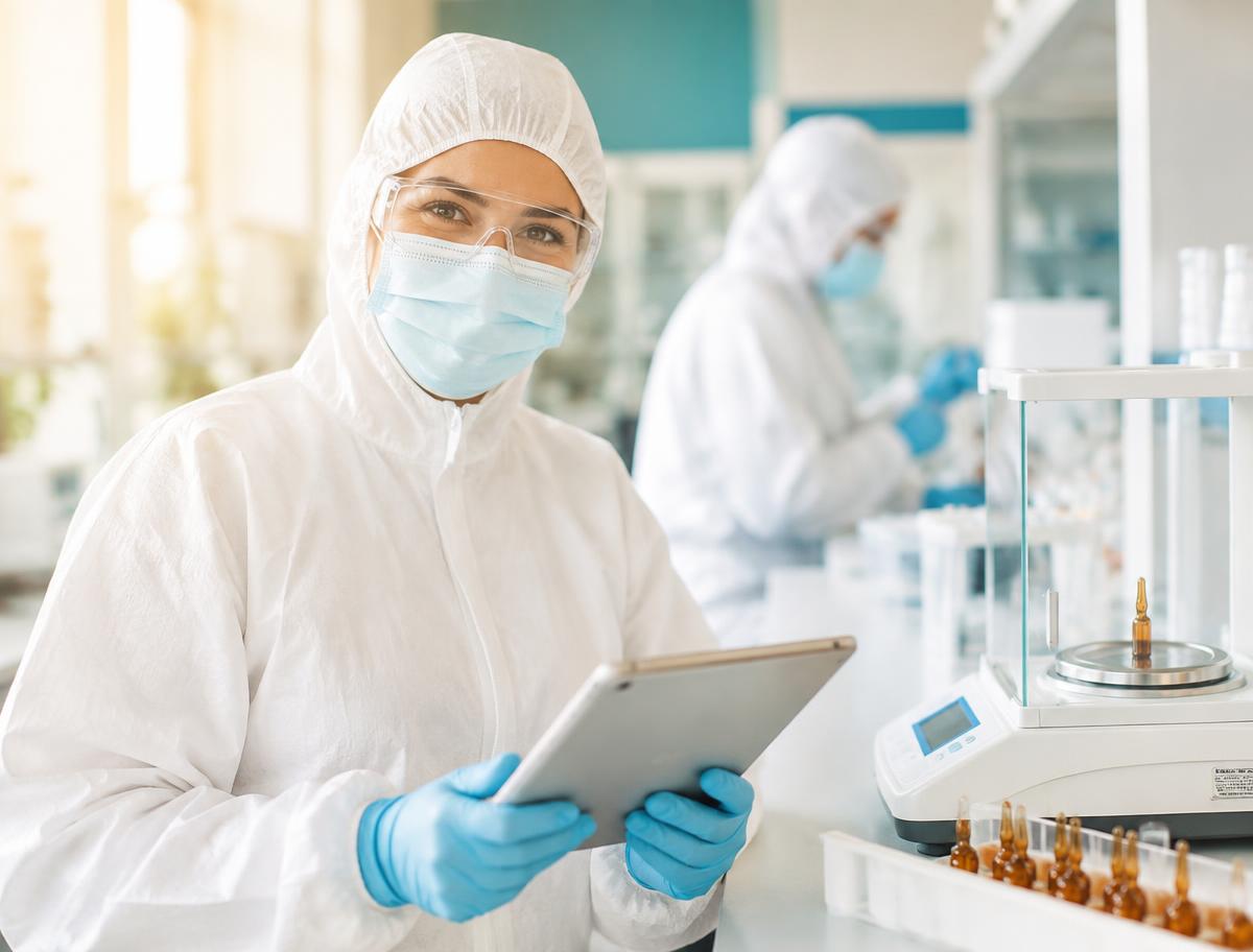 Smiling reference materials & standards team member in full protective clothing using a tablet on the production floor