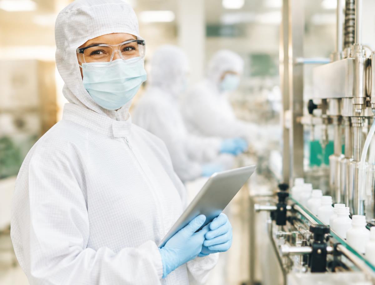 Smiling veterinary pharma team member in full protective clothing using a tablet on the production floor
