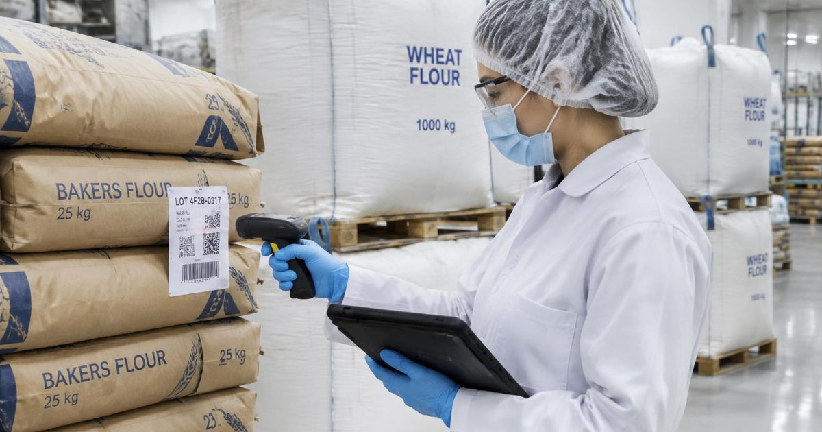 Protected bakery worker scanning a flour sack beside bulk bags