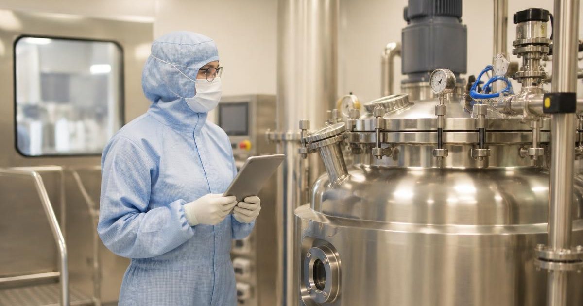 EU GMP Annex 15 qualification: a gowned validation engineer reviews equipment qualification on a tablet beside a stainless steel vessel
