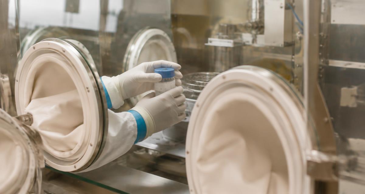 Gloved hands handling a sealed container inside a containment isolator